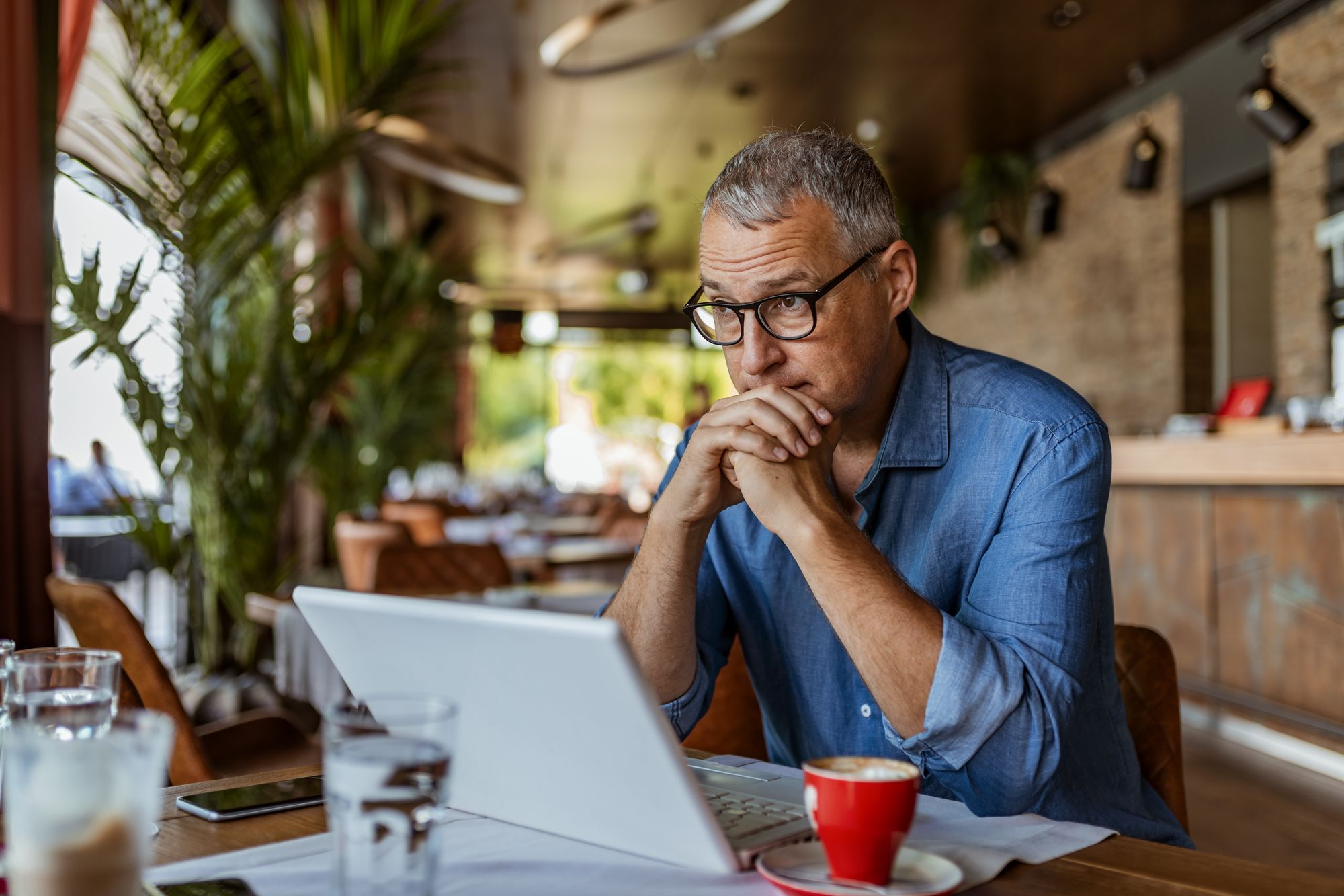 An experienced business owner in thought, laptop open in a café